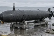 Generic torpedo-shaped autonomous underwater vehicle resting on a cradle on a quayside, with cross-form tail fins and a short transparent mast