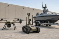 Generic quadcopter, small uncrewed ground vehicle and uncrewed surface vessel arranged on a concrete apron under flat daylight, no markings