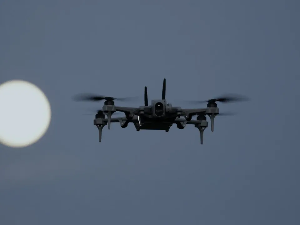 Teal 2 dark grey quadcopter with two antennas and a gimbal camera, hovering against a dusk sky with the full moon to its left