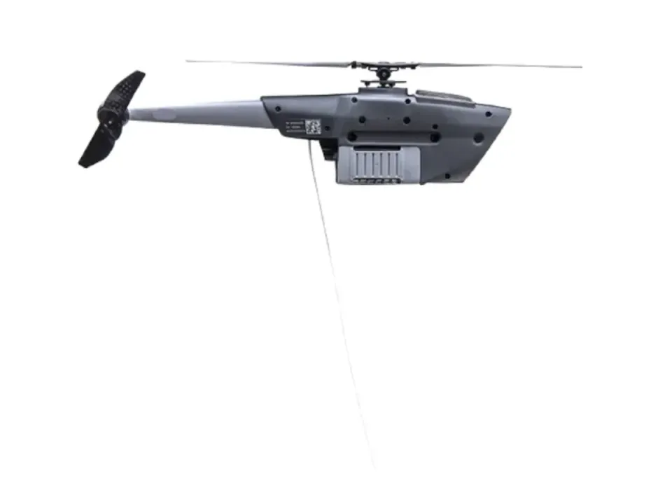 Black Hornet 4 nano-helicopter drone in side view, grey body with a camera pod under the nose and a thin tail rotor, on a white background