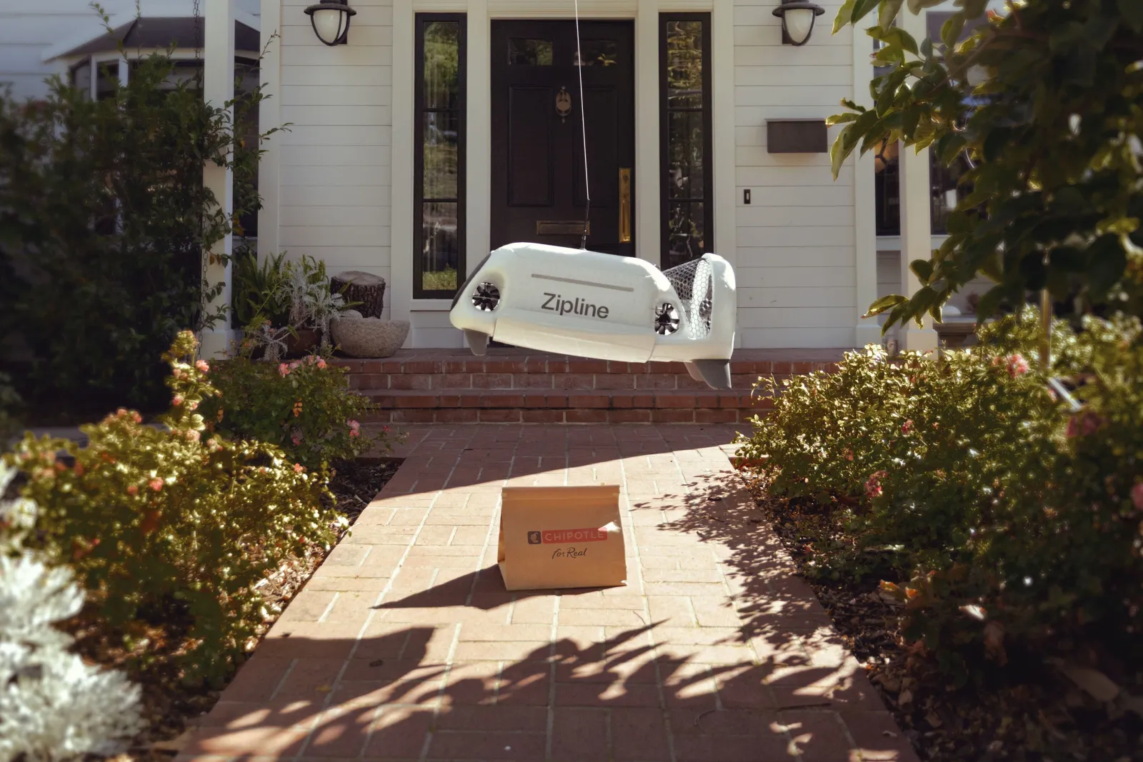 Zipline Platform 2 drone lowering a Chipotle food order via tether in a residential Texas neighborhood